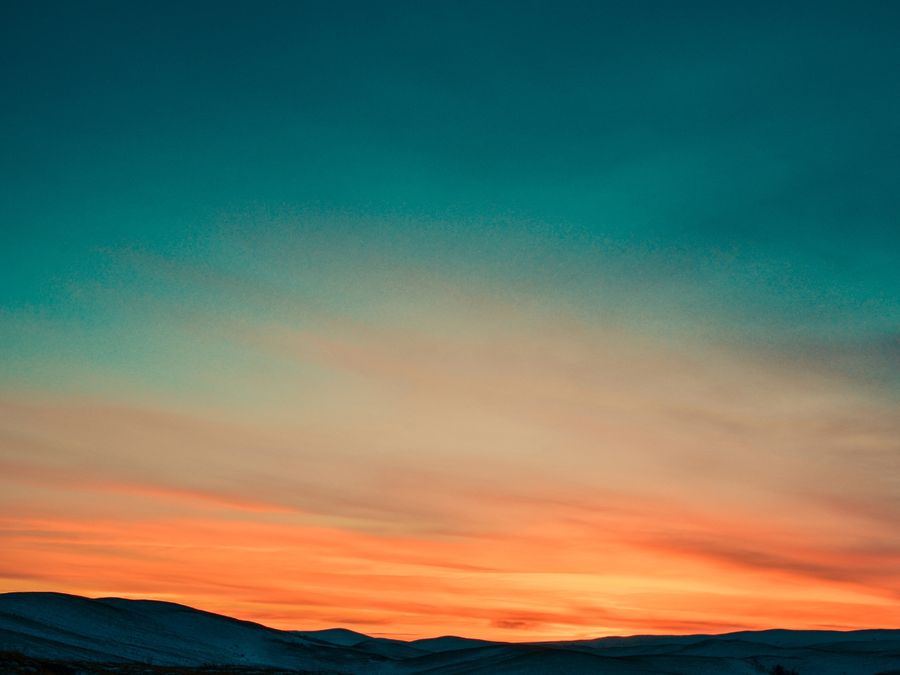Teal-to-orange sunset over dark hills